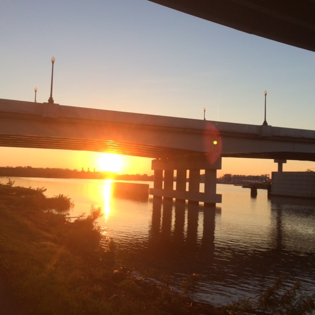 The sun is setting over a bridge over a body of water.