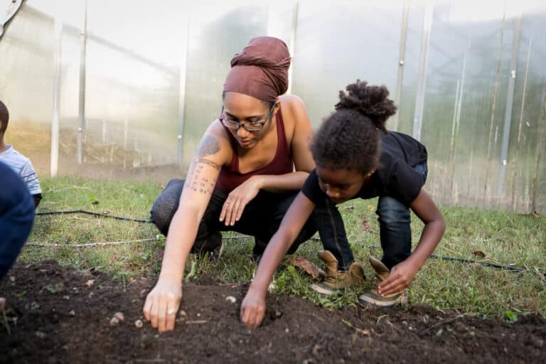 A woman and a girl planting a dirt patch.