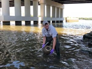 A man holding a bucket in the water under a bridge.