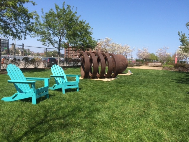 Two blue chairs sit in the grass next to a sculpture.