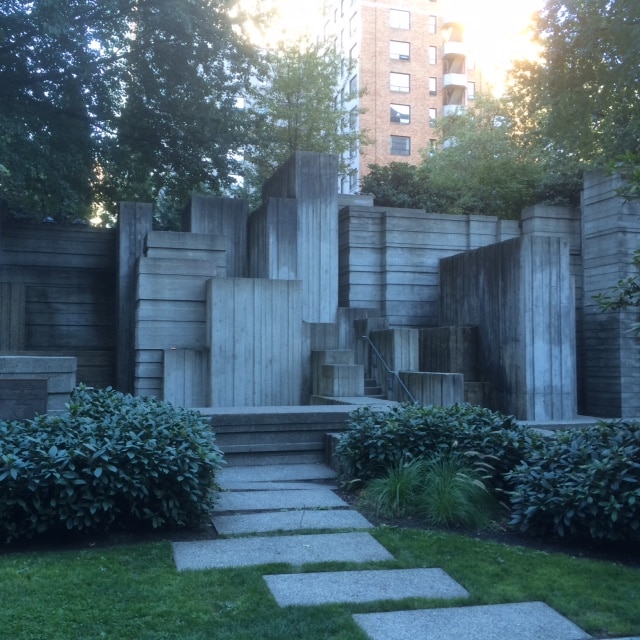 A concrete garden in a city with trees and shrubs.