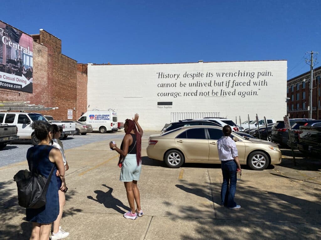 A group of people standing in front of a building with a quote on it.