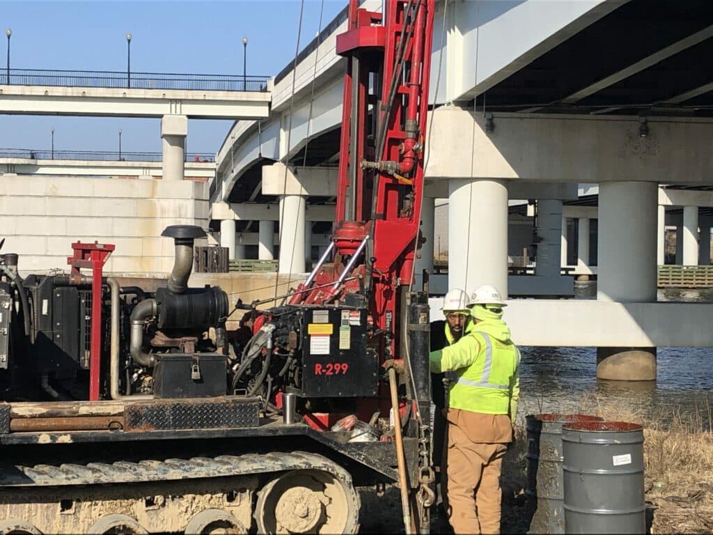 A man is working on a machine under a bridge.
