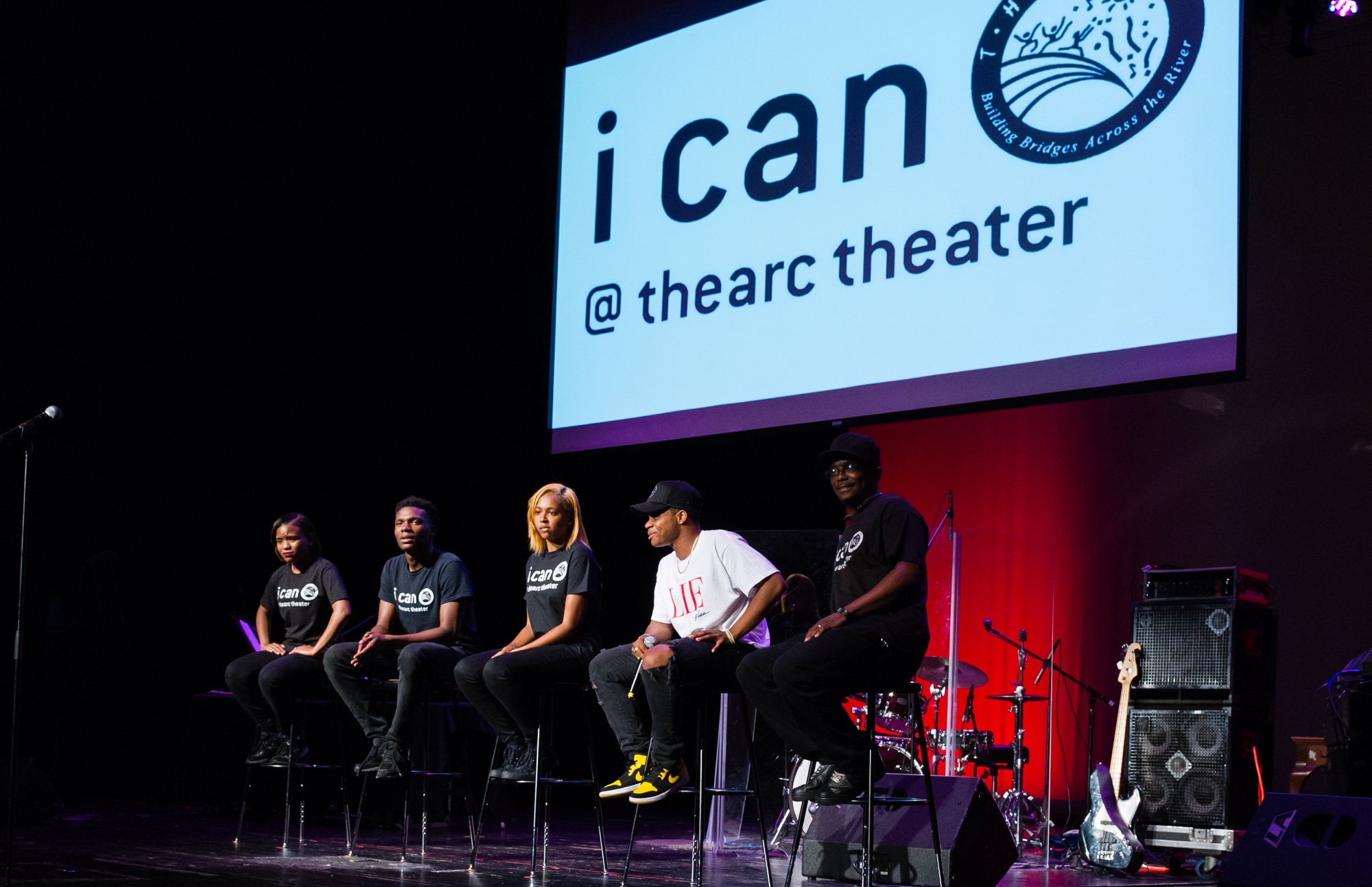 A group of people sitting on stools in front of a sign that says iCAN Technical Theater Internship, empowering African American youth in DC.