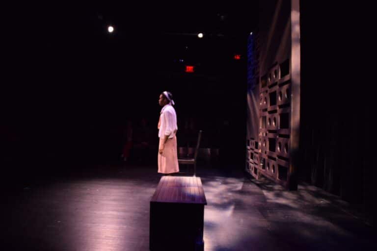 A woman standing on a bench at THEARC Theater, promoting arts and community engagement in a dark room.