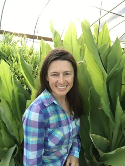 A woman smiles while standing among large green plants in a greenhouse, embodying the spirit of building a better future.