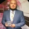 A man in a blue suit holds an award while standing against a colorful background resembling an urban street scene, symbolizing his dedication to Building a Better Future.