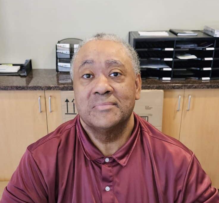 A person wearing a maroon shirt sits at a desk with a laptop in the Town Hall Education office, focused on a project aimed at Building a Better Future.