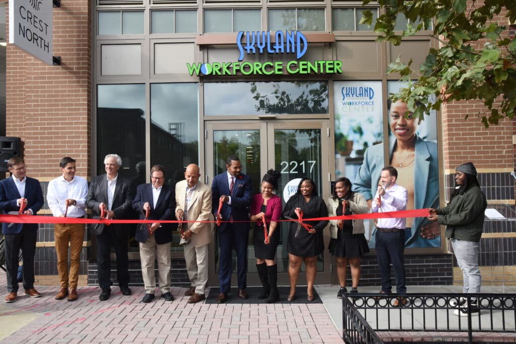 A group of people participate in a ribbon-cutting ceremony in front of Skyland Workforce Center.