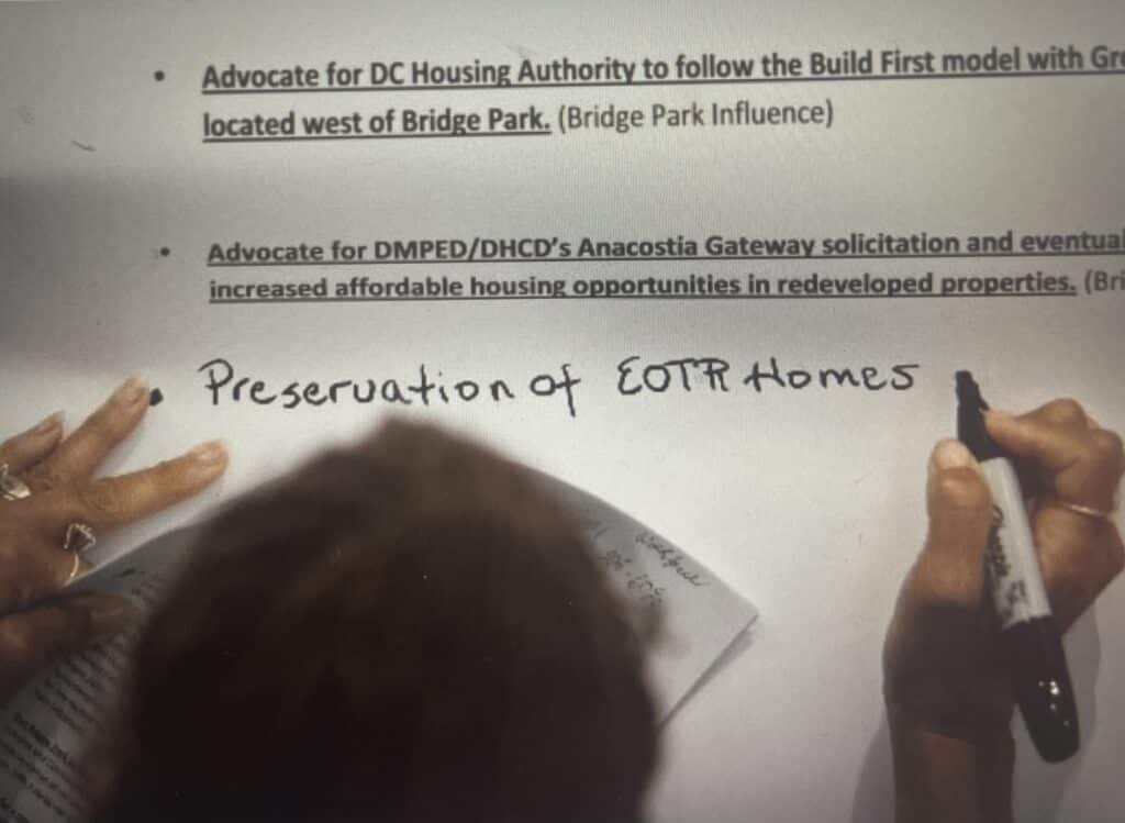 A person writes "Preservation of EOTR Homes" on a document with a marker, surrounded by printed text.