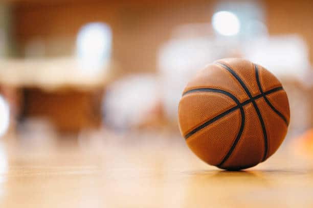 A basketball rests on a gym floor with a blurred background.