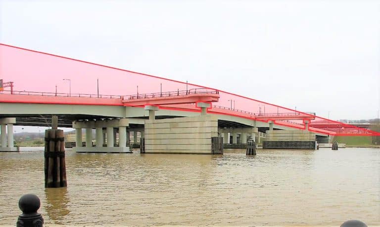 A multi-lane bridge stretches over a body of water, its top structure accented by a red highlighted area, embodying our "Building Bridges Across The River - Our Story" theme. The calm water beneath and cloudy skies above reflect our commitment to community-driven design.