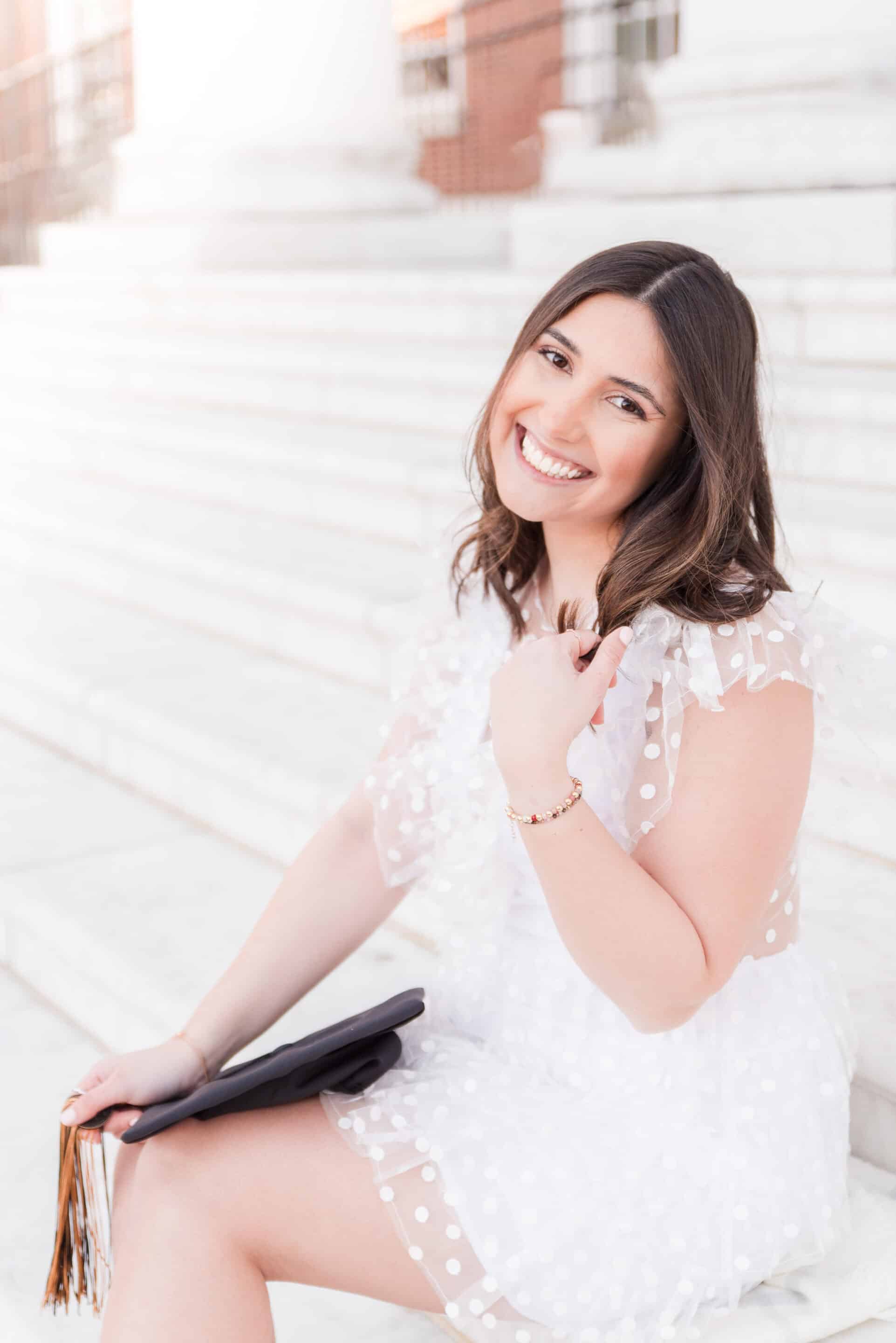 A woman in a white polka dot dress sits on marble steps, smiling and holding a black folder, embodying the spirit of building a better future.