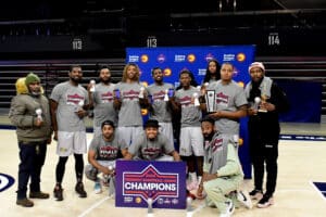 A basketball team poses on the court holding trophies, with a "Champions" banner in front of them.