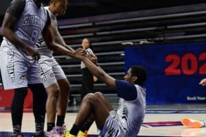 Basketball players in gray uniforms assist a teammate up from the floor during a game.