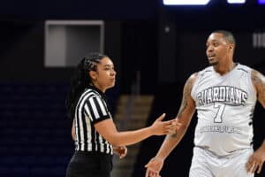 A referee and a basketball player in a "Guardians" jersey are engaged in a discussion on the court.