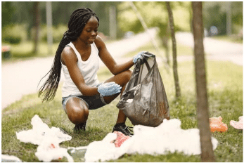 Person wearing gloves picks up trash and puts it in a black garbage bag in a park.